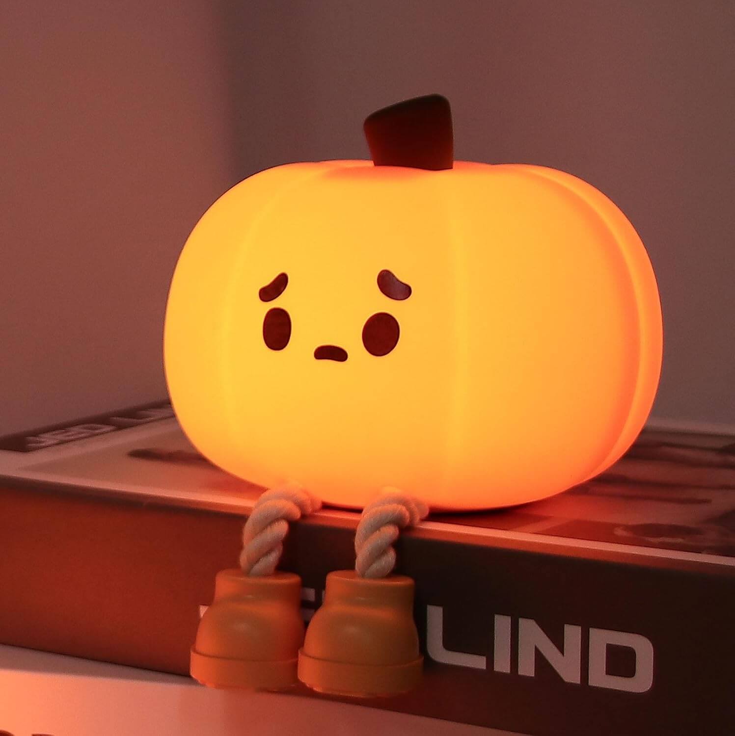 Cute pumpkin nightlight with a sad face, sitting on a box, illuminating a warm glow.